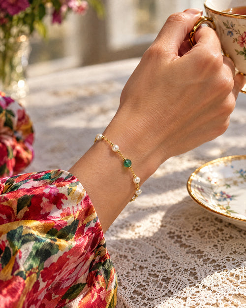 Bracelet Perles worn on a wrist holding a porcelain teacup, a floral silk sleeve behind