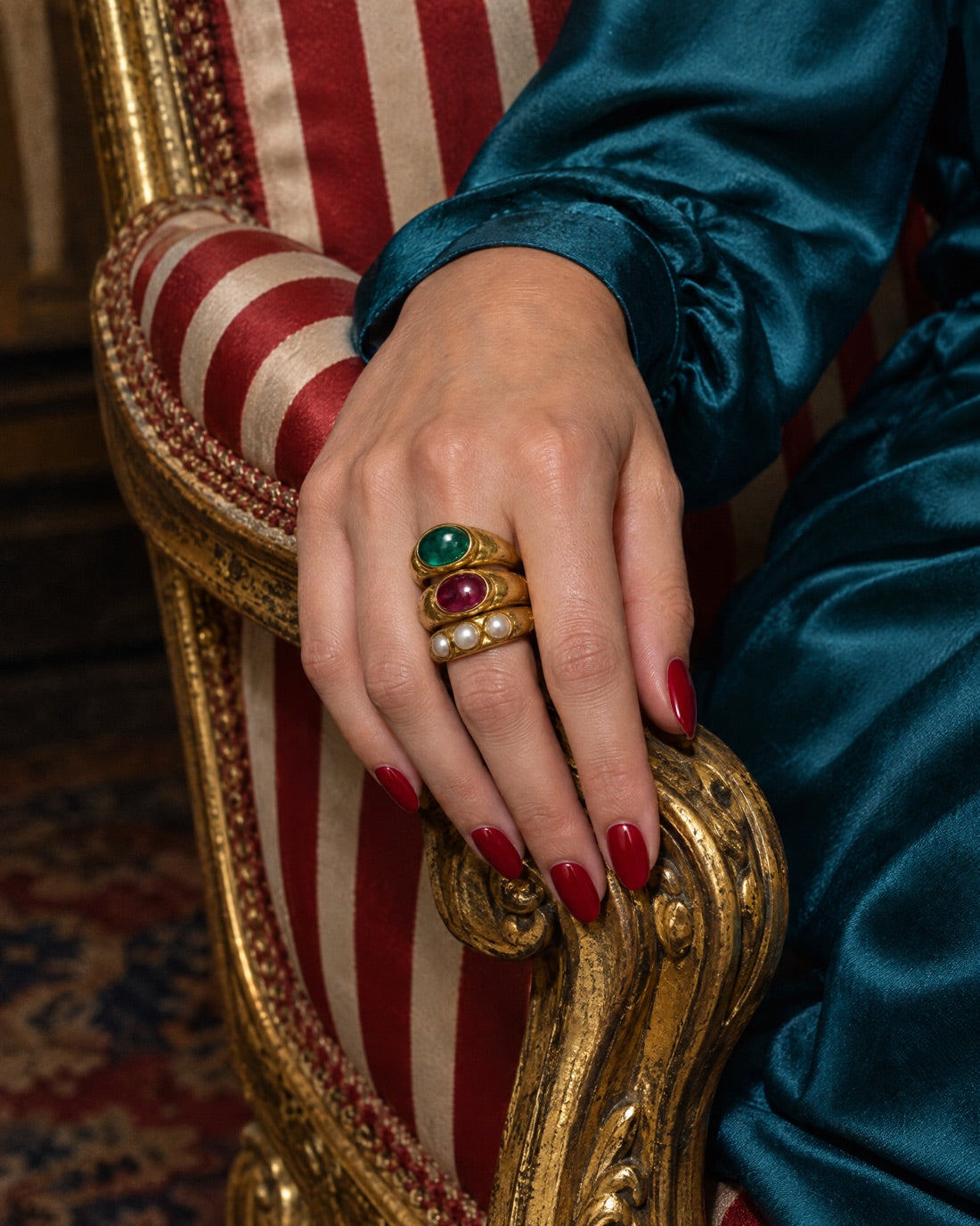 The three rings worn stacked on a hand resting on a striped salon chair