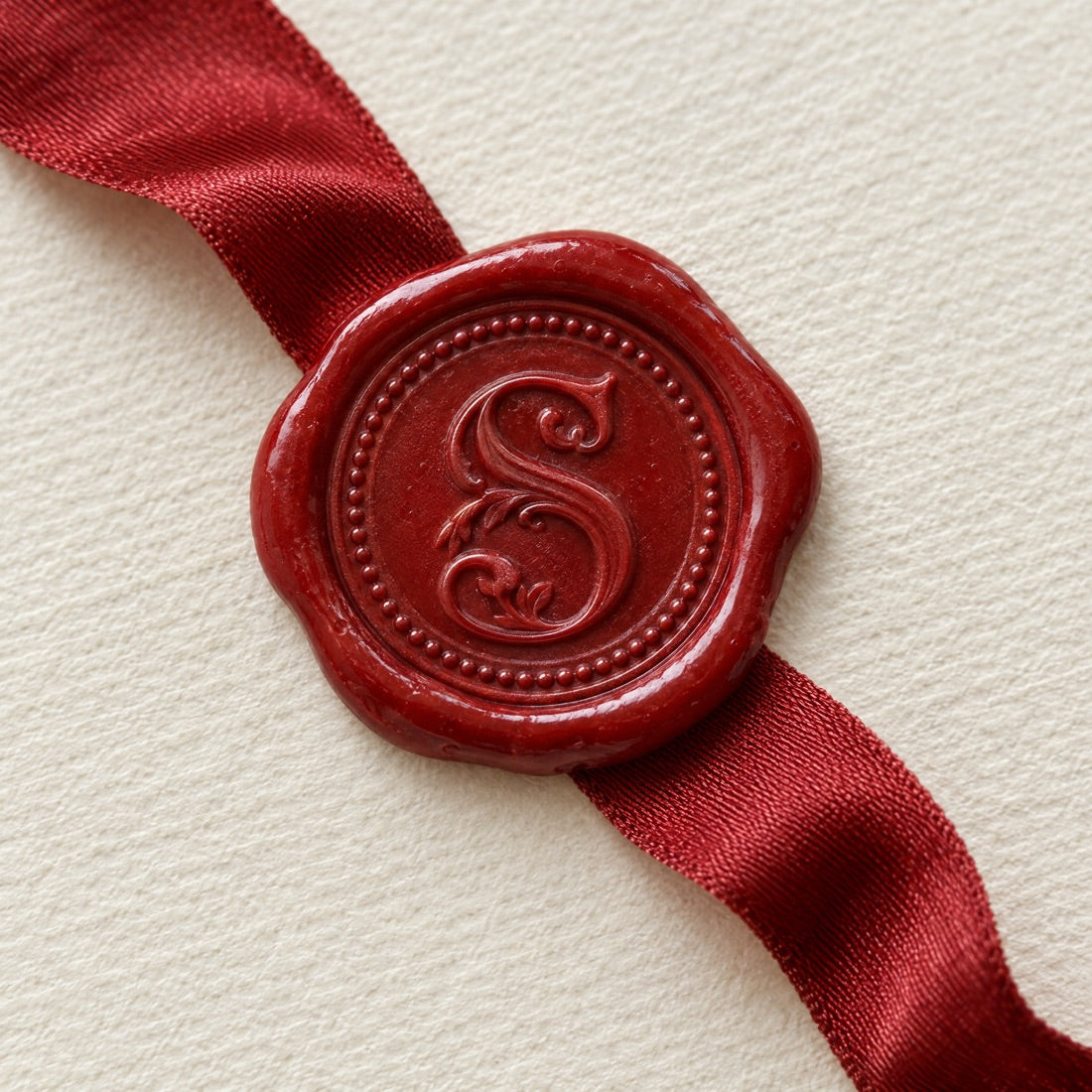 A red wax seal pressed with the Sabelle S on a red satin ribbon over cream paper